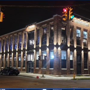 Night view of a The Silk Factory, a well-lit, two-story brick building on a street corner with traffic lights.