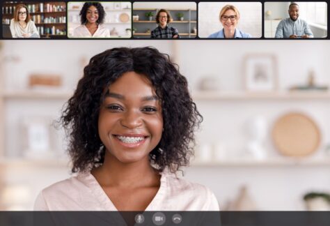 A smiling woman during a video conference call with five other participants.