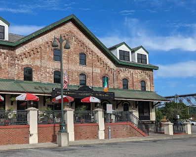 A two-story brick building with a green awning and outdoor seating under red umbrellas.