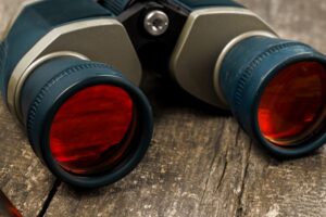 Close-up view of a pair of binoculars with red lenses on a wooden surface.