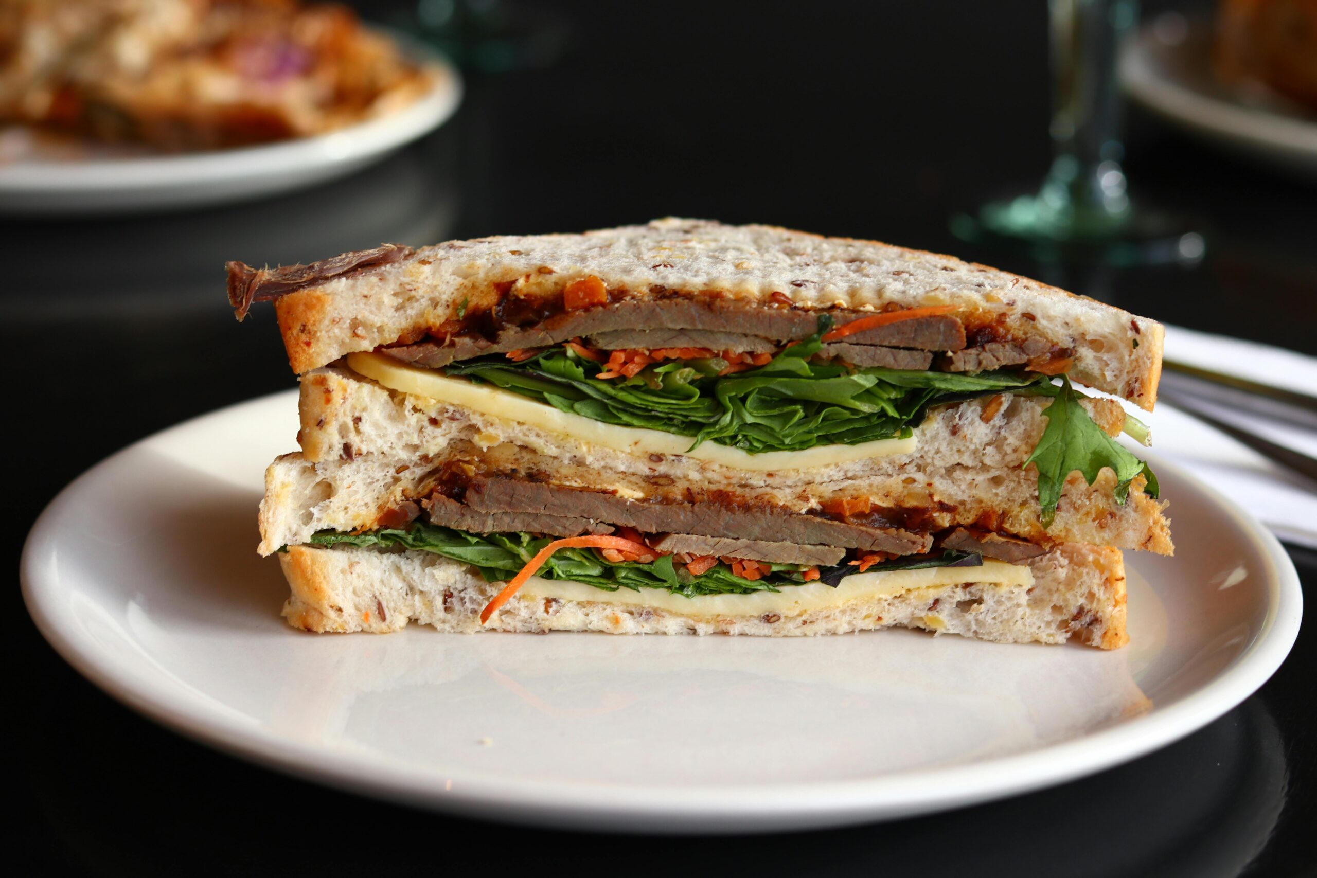 A close-up image of a sandwich with layers of turkey, cheese, spinach, and tomato on a white plate.