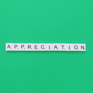 White Scrabble tiles spelling "APPRECIATION" are arranged in a horizontal line against a green background.